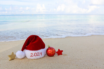 New Year 2024 background with Christmas hat and decorations on Caribbean sand.