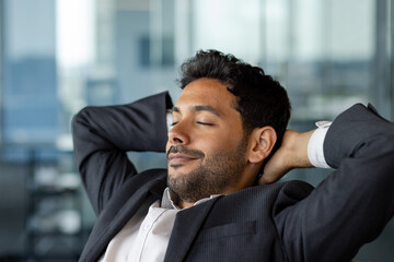 Young male businessman close-up resting in office, boss in business suit with hands behind head...