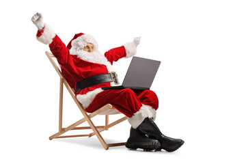 Happy santa claus sitting on a deck chair and using a laptop computer