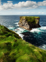 Fototapeta na wymiar View on rough small island in the ocean from a cliff, Ireland, Kilkee area. Warm sunny day, blue cloudy sky. Travel, tourism and sightseeing concept. Irish landscape and coastline.