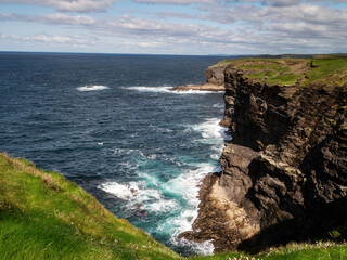 Stunning scene with cliffs, rough stone island, ocean and blue cloudy sky.