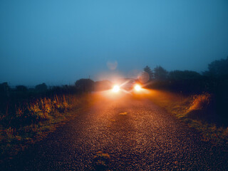 Car illuminating small narrow country road in a fog. Poor visibility due to hard weather condition....