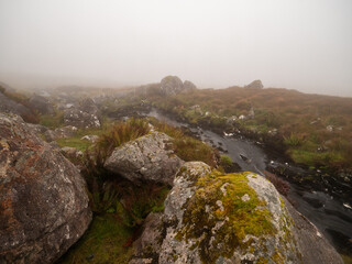 Irish nature scene with small creek in green fields with rocks and fog in the background. Connemara, Ireland. Hard weather conditions. Nature, travel and sightseeing.