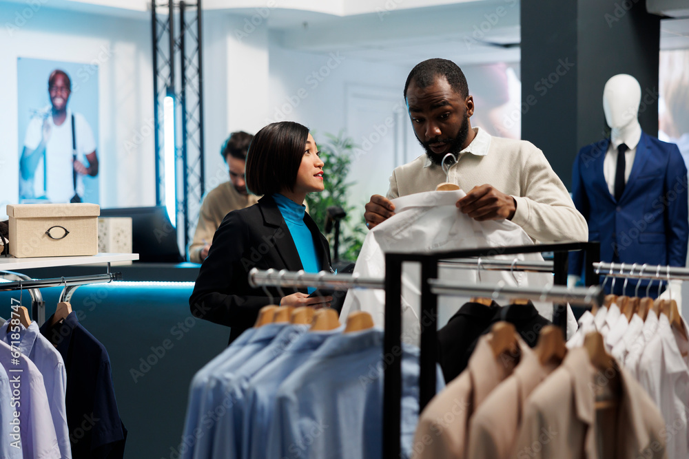 Wall mural clothing store african american customer holding shirt on hanger, discussing style and fit with cons