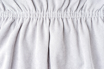 White corduroy fabric gathered with elastic close-up. Velveteen texture with folds and drapery. Cloth surface, textile background, wallpaper, backdrop.