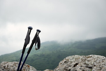 Blue hiking poles sticking out from the cliff edge with moody, dark, stormy sky in the background - 671859921