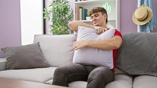 Worried young hispanic man suffering from severe stomachache, unhappily touching his abdomen while resting on a living room sofa in his apartment, portraying a picture of indoor illness.