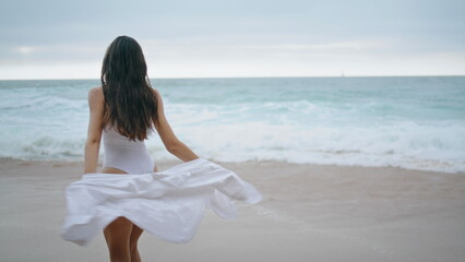 Woman spinning sandy beach wearing white sexy swimsuit. Girl walking seashore.