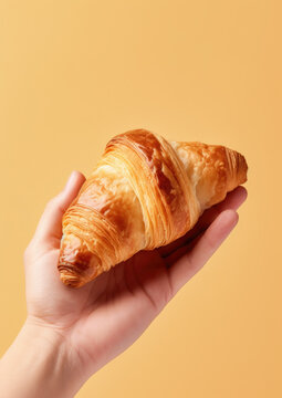 Hand holding a croissant on flat yellow background. AI generative.