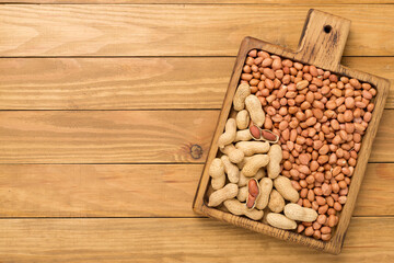 Peeled and unpeeled peanuts on wooden background, top view