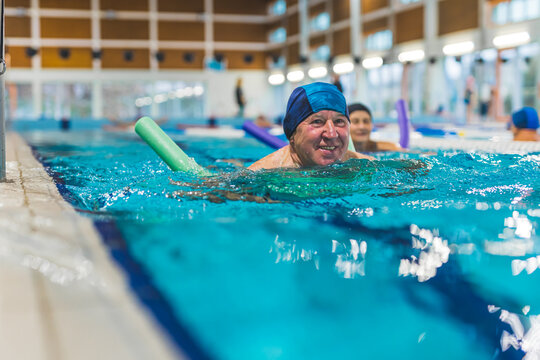 smiling senior Caucasian man with blue swimming cap using a swim noodle in the pool. High quality photo