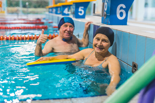 senior woman holding a yellow kickboard in the pool and her husband showing a thumb-up. High quality photo