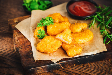 Breaded chicken nuggets. Semifinished chicken nuggets from chicken fillet on a dark background with fresh herbs. Quick cooking at home. Fast food. Breaded Chicken Inner Fillet.