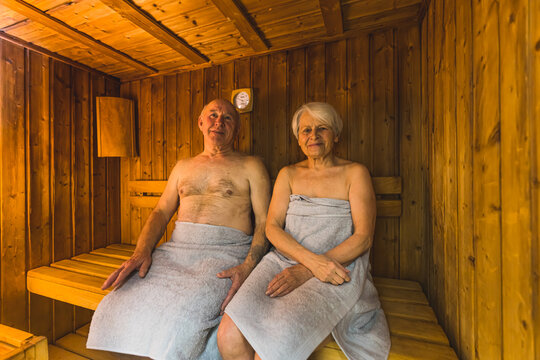 aged Caucasian couple with towels sitting in the wooden sauna and smiling, medium full shot, well-being concept. High quality photo