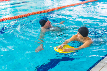 old Caucasian woman learning to swim by a kickboard with her husband in the pool. High quality photo