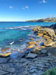 Rocky coast of the ocean. Bay and coastline. View of the city in the distance. View of turquoise waves breaking on the shore. Landscape and shore. Australia, 