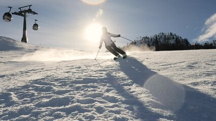 LENS FLARE, SLOW MOTION: Lady sprays snow into camera while skiing on ski piste. Experienced female skier is carving on the slope of ski resort in snowy Austrian Alps. Nice sunny day for winter sports - Powered by Adobe