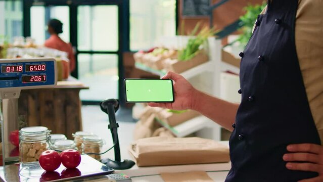 Merchant with phone greenscreen at store counter, presenting isolated chromakey display on mobile gadget. Farmer and vendor using modern copyspace template with mockup technology.