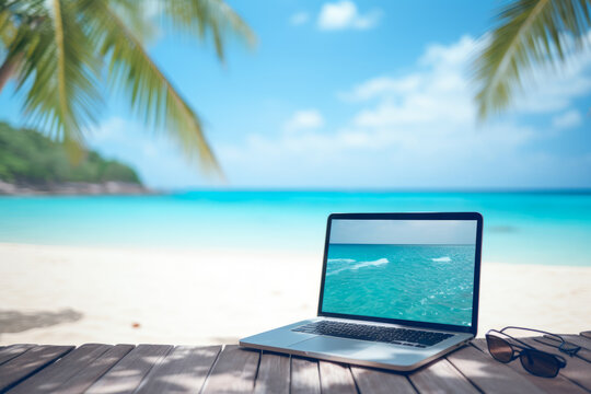 Laptop computer on a wooden table in the shade of a palm tree. A photo of a white sandy beach and an emerald green tropical beach taken with a smartphone. Concept for holidays and vacation.
