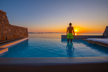 Fototapeta premium Tourist enjoys at the infinity swimming pool villa at sunset time, Mykonos, Greece
