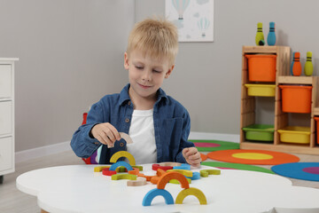 Motor skills development. Boy playing with colorful wooden arcs at white table in kindergarten