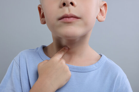 Endocrine system. Little boy doing thyroid self examination on light grey background, closeup
