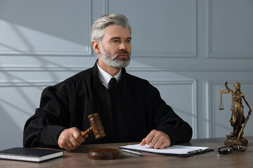Judge with gavel and papers sitting at wooden table indoors