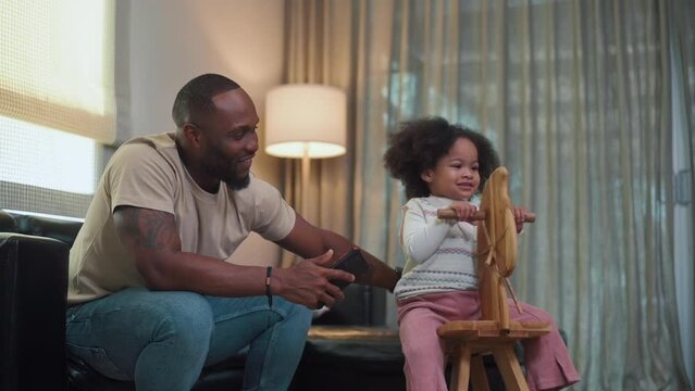 Happy African American man playing with his daughter in living room at home