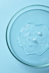 Petri dish with sample of cosmetic oil on light blue background, top view
