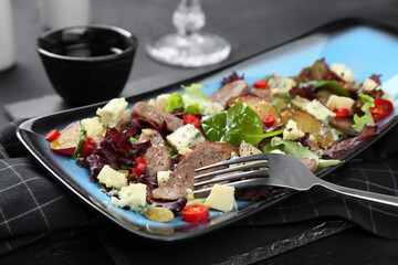 Delicious salad with beef tongue, cheese and fork served on black table, closeup