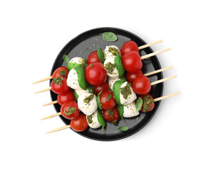Plate of Caprese skewers with tomatoes, mozzarella balls, basil and pesto sauce isolated on white, top view