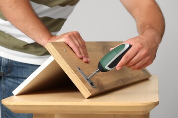 Man with electric screwdriver assembling furniture at table indoors, closeup