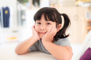 5-6 years old, cute Asian girl sitting with her hand on her chin and smiling while waiting to eat...