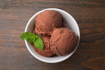 Bowl with tasty chocolate ice cream and mint leaves on wooden table, top view