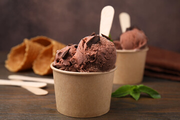 Paper cups with tasty chocolate ice cream on wooden table, closeup