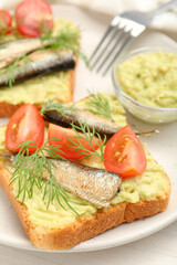 Delicious sandwiches with sprats, tomatoes, dill and avocado puree served on white table, closeup