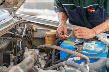 A mechanic tightens the battery terminals with a wrench.