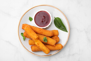 Tasty fried mozzarella sticks served with tomato sauce and basil on white marble table, top view