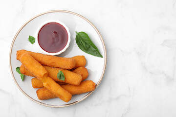 Tasty fried mozzarella sticks served with tomato sauce and basil on white marble table, top view. Space for text