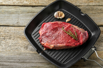 Grill pan with piece of raw beef meat, garlic and thyme on wooden table