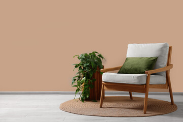 Stylish armchair with cushion and green plant near beige wall indoors, space for text