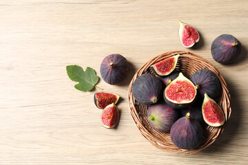 Whole and cut ripe figs with leaf on wooden table, flat lay. Space for text
