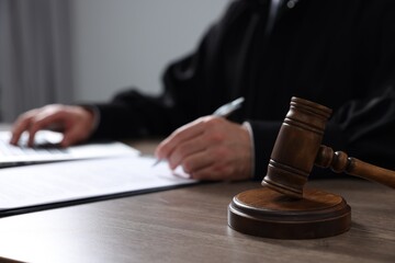 Judge with gavel writing in papers at wooden table, closeup - obrazy, fototapety, plakaty