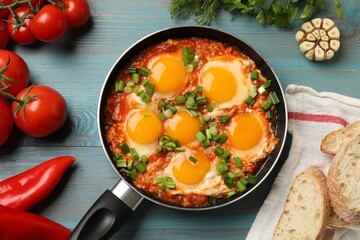 Delicious Shakshuka in frying pan served on light blue wooden table, flat lay