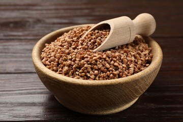 Bowl and scoop with dry buckwheat on wooden table, closeup