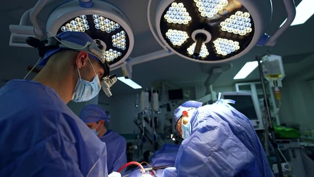 Team of neurosurgeons perform operation in modern operational theatre. Doctors wear device glasses at surgery.