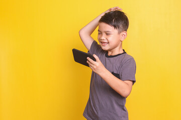 Little boy playing online game on smartphone gesturing disappointed expression isolated on yellow background  - obrazy, fototapety, plakaty
