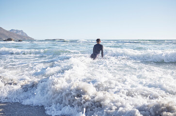 Surfing, man and swimming in sea waves, ocean and summer on blue sky in Cape Town, South Africa....