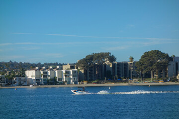 Fast moving motorboat with a trail of sparkling waves across Mission Bay in front of resort style housing in San Diego, California
