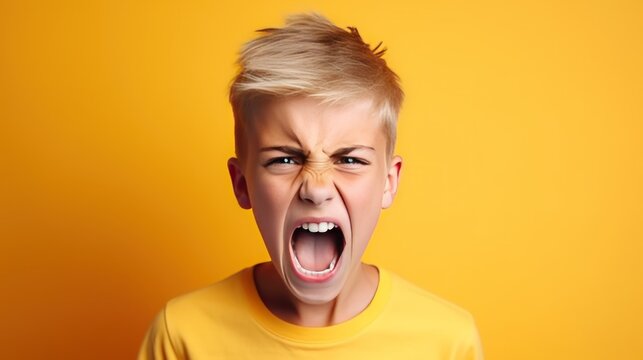 Angry irritated boy on yellow background. Full of rage. Emotional portrait of an upset preteen boy screaming in anger. Requirements for parents. Wrong perception. Hysterics.